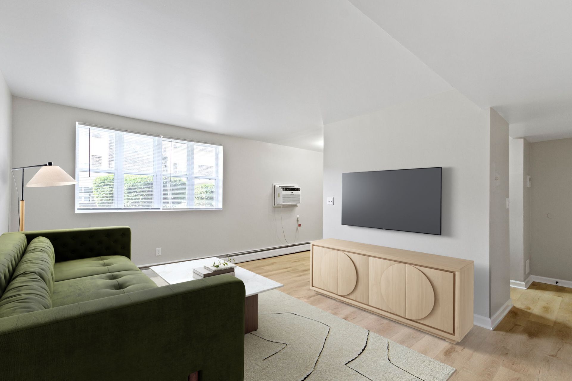 Green couch in a bright living room with a mounted TV and wood cabinet.