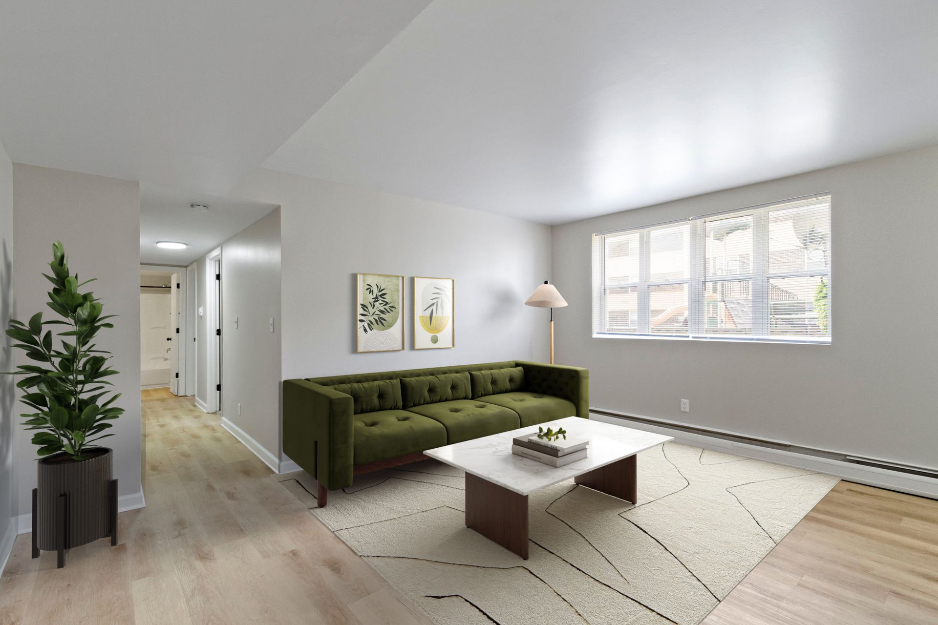 Living room with green sofa, white rug, and artwork. Natural light from window.