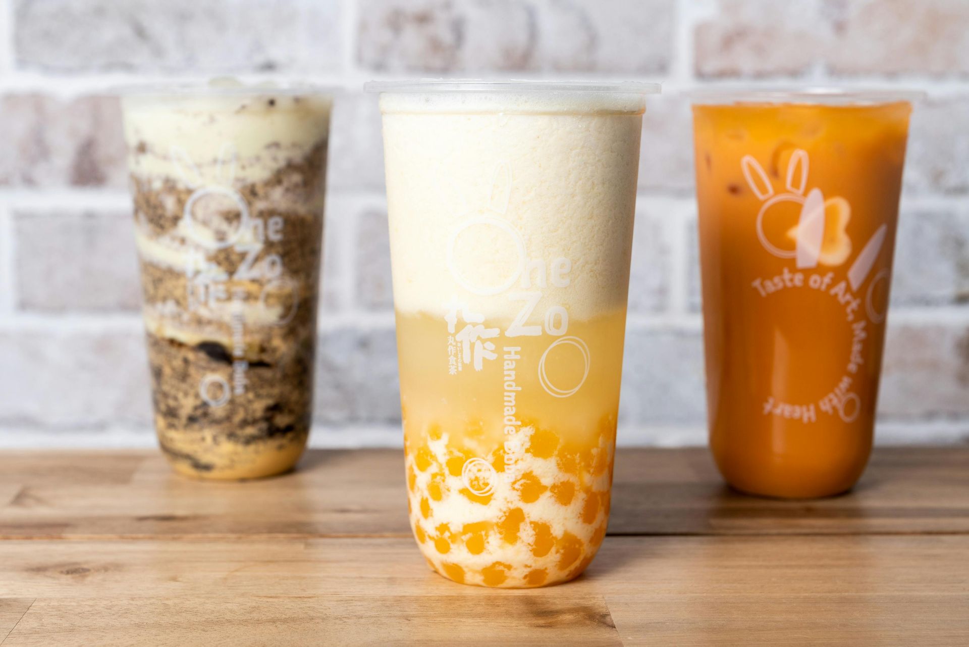 Three bubble tea drinks on a wooden surface: chocolate, yellow pineapple, and orange Thai tea.