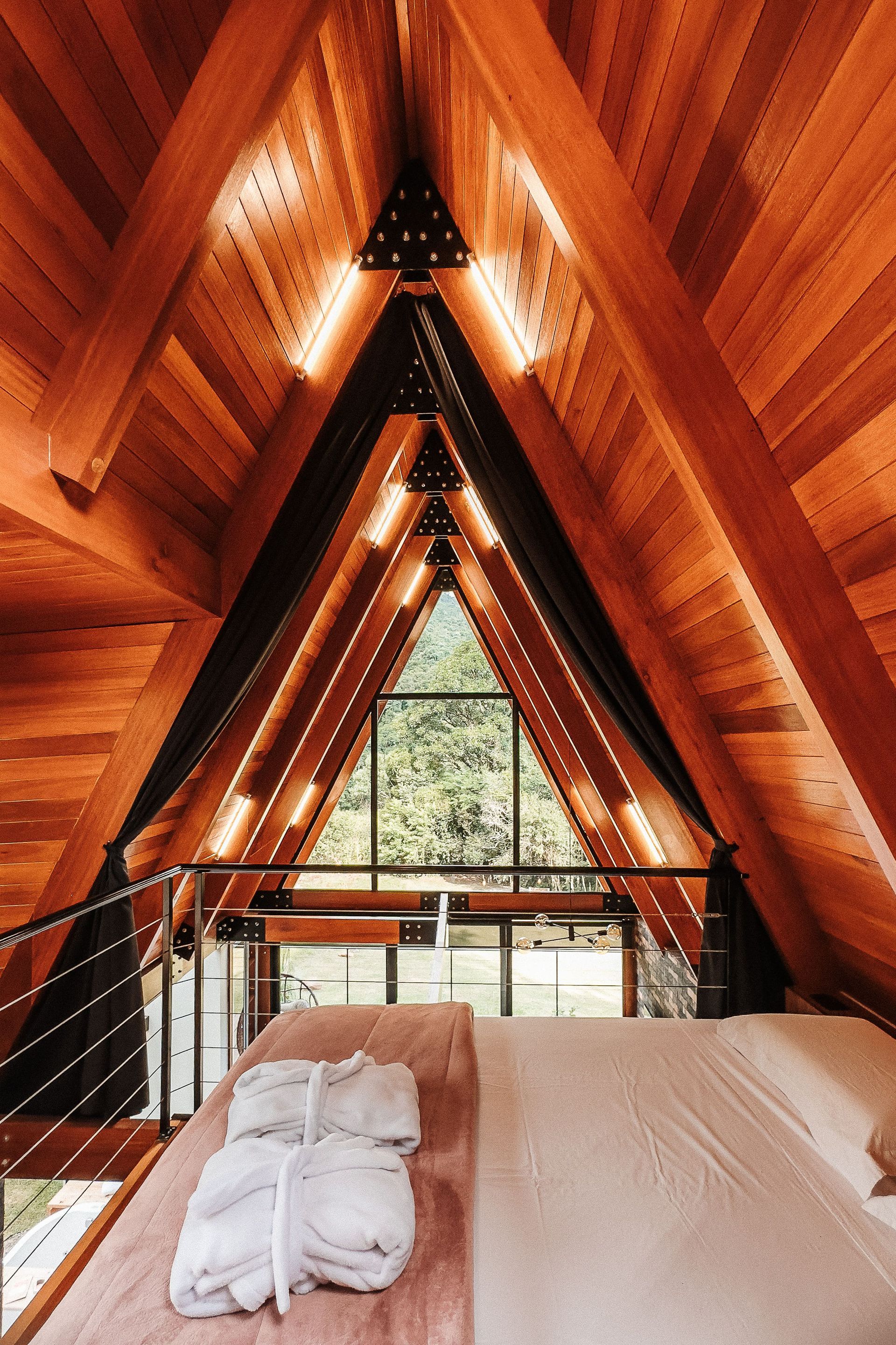 Interior de uma cabana de madeira em forma de A com cama, janela e roupão.