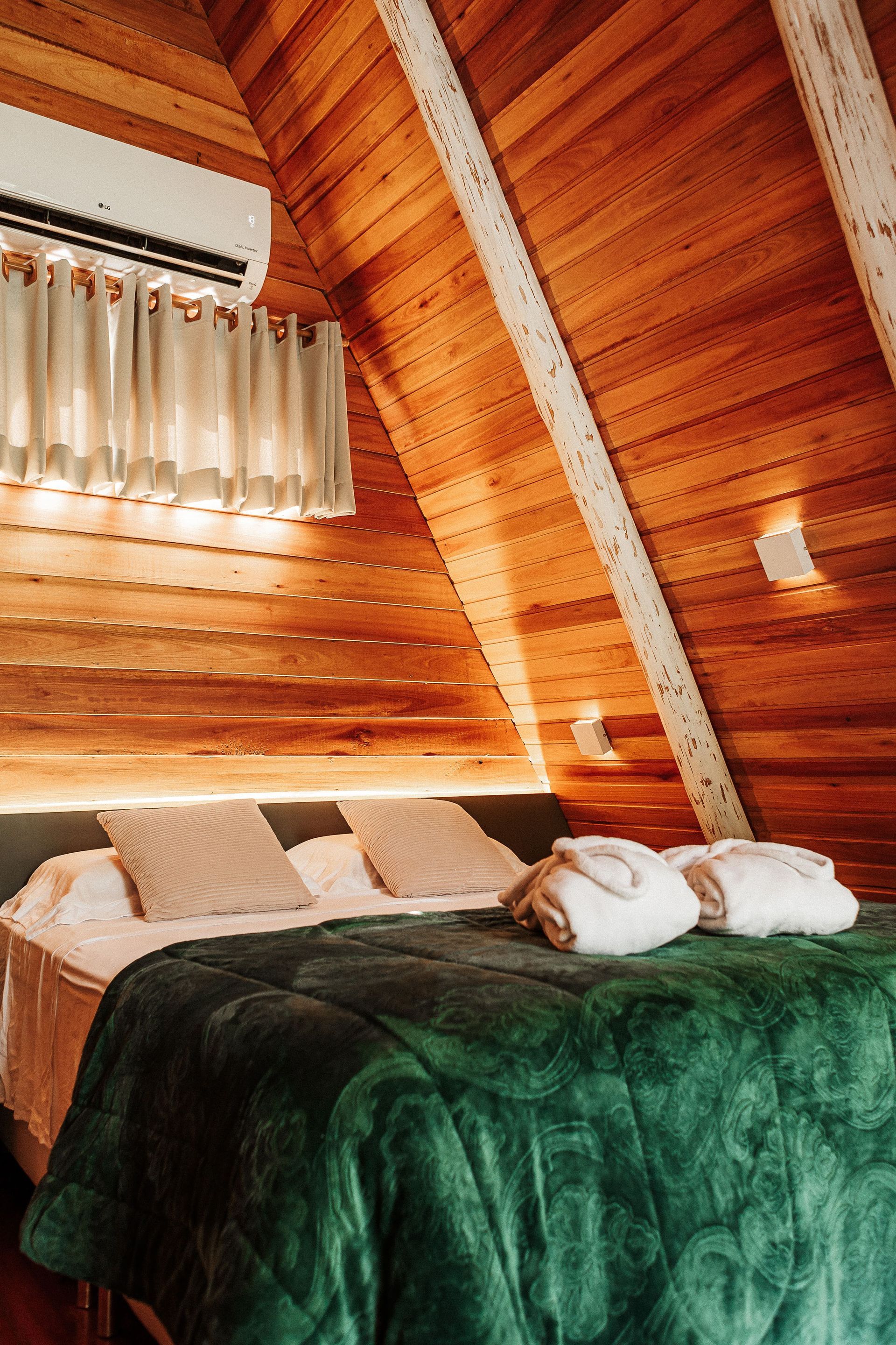 Quarto aconchegante em formato de A com painéis de madeira, cama com edredom verde, dois roupões e ar condicionado.