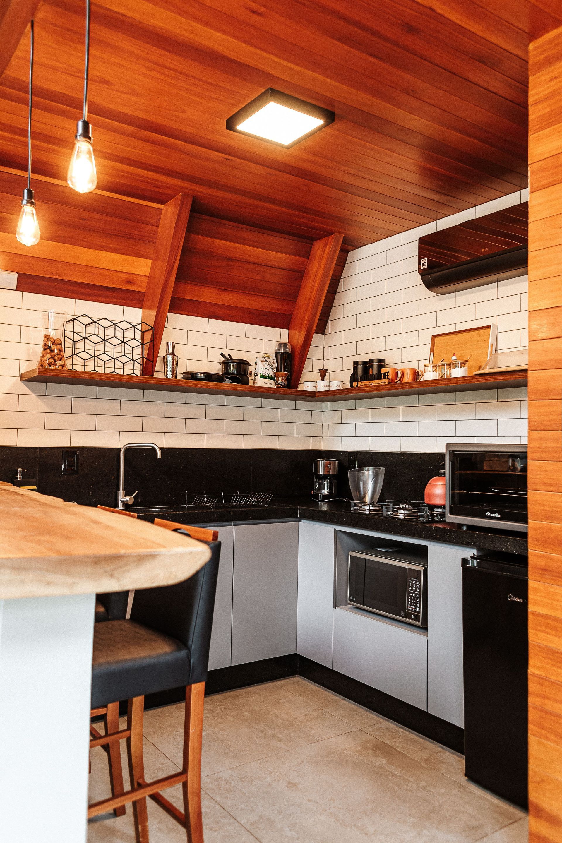 Cozinha pequena e moderna com teto de madeira, bancadas pretas e armários cinza.