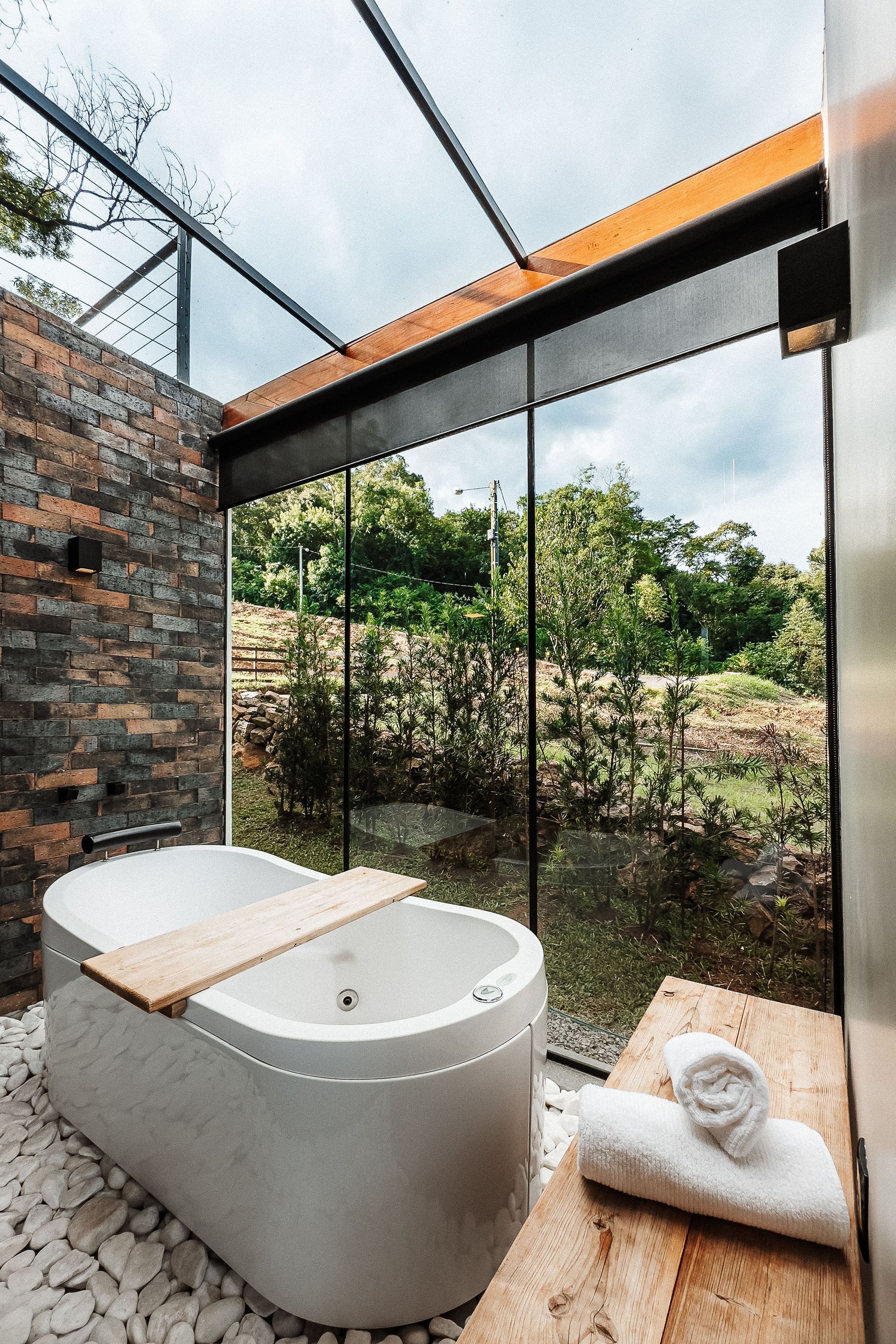 Banheiro moderno com banheira, janela ampla com vista para a vegetação, paredes de pedra e detalhes em madeira.