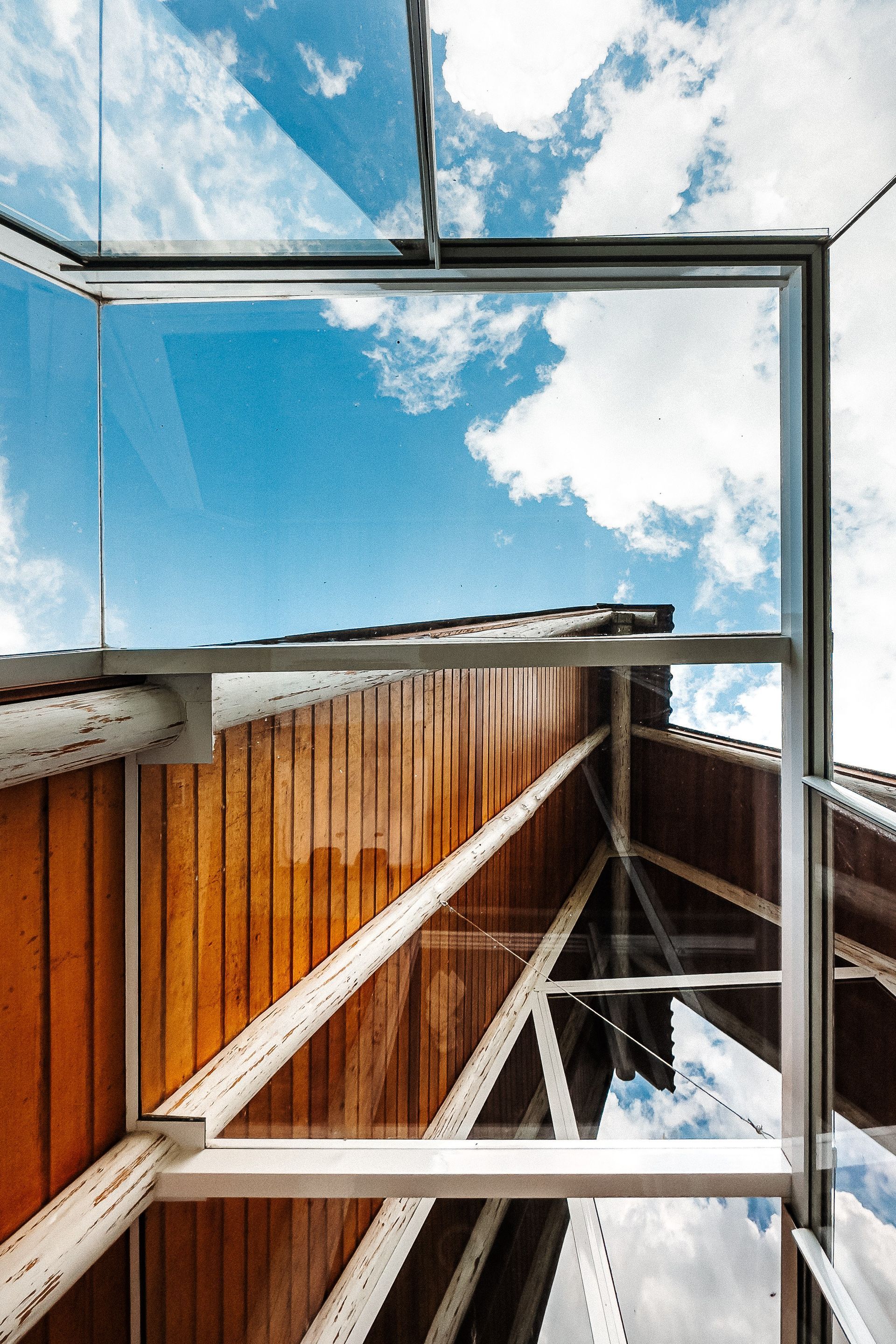 Olhando através das janelas de vidro para o céu azul e o teto de madeira com vigas brancas.