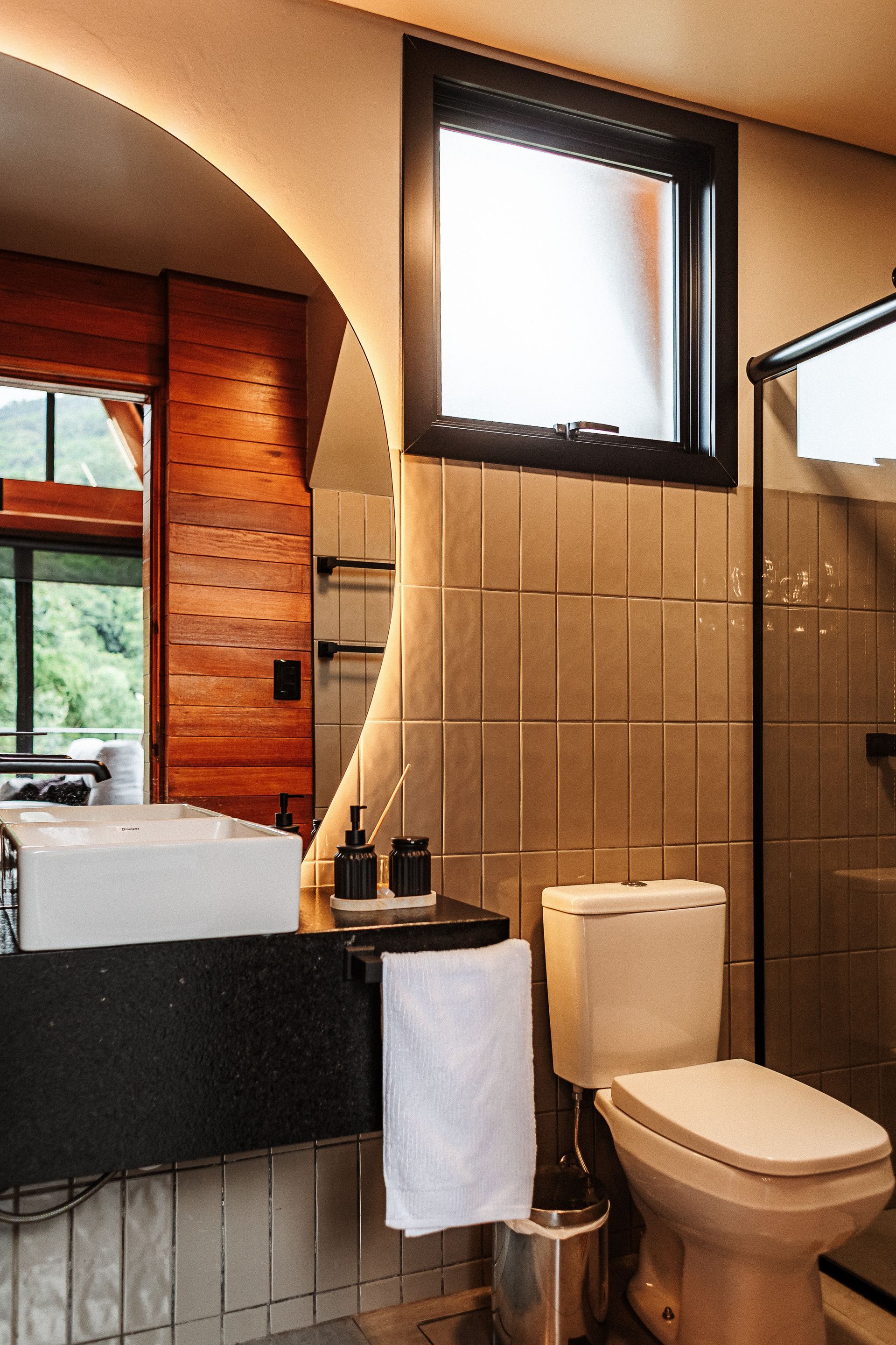 Banheiro com um grande espelho redondo, detalhes em madeira e uma pequena janela.