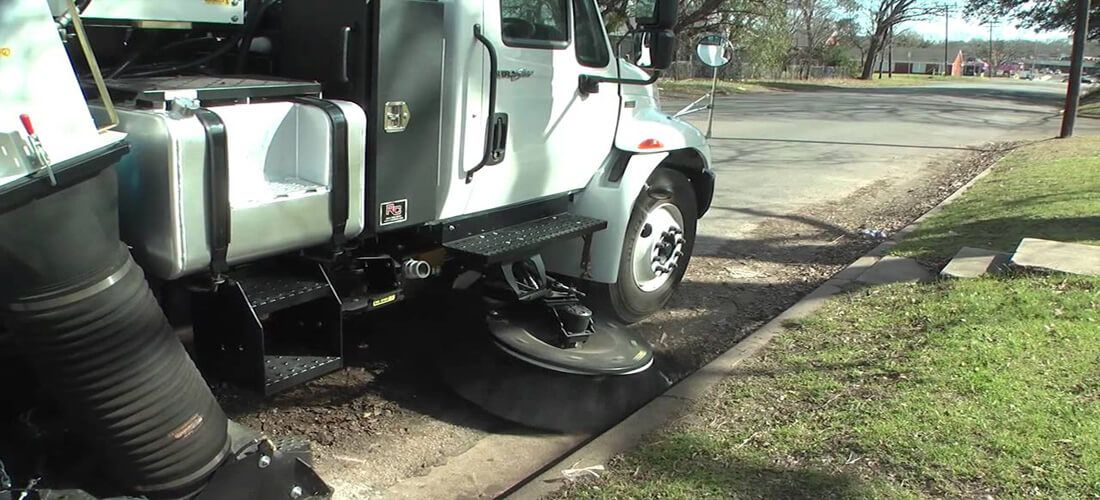A street sweeper is cleaning the sidewalk on a sunny day.
