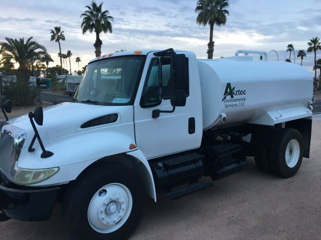 A white tanker truck is parked in front of palm trees