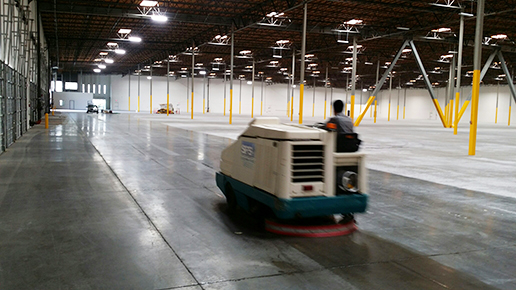 A man is riding a cleaning machine in an empty warehouse.