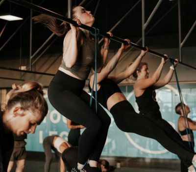 Women doing pull-ups with resistance bands in a gym. Black leggings, neutral tops, and determined expressions.