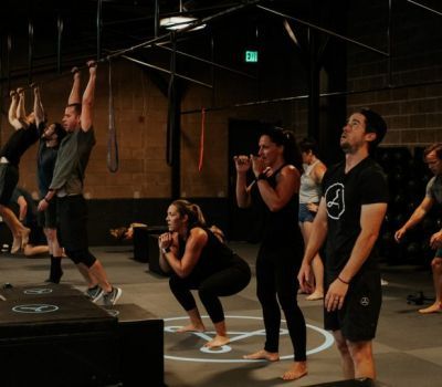 Group fitness class: People exercising in a gym. Some squat, punch, hang from bars, and lift.