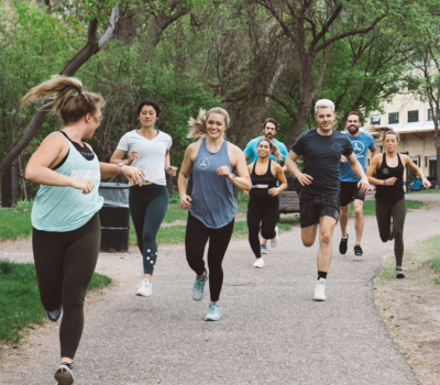 Group of people running on a path in a park. They wear athletic clothing and appear to be exercising.