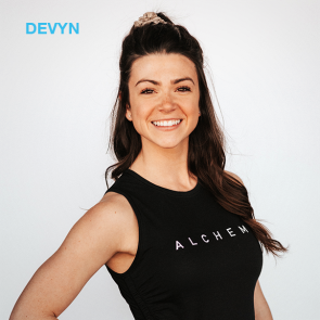 Devyn smiles wearing a black tank top with "ALCHEM" and a scrunchie, in front of a white background.