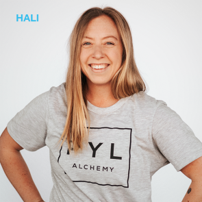 Woman with blonde hair, smiling, wearing a gray t-shirt with "NYL Alchemy" and arms at sides.