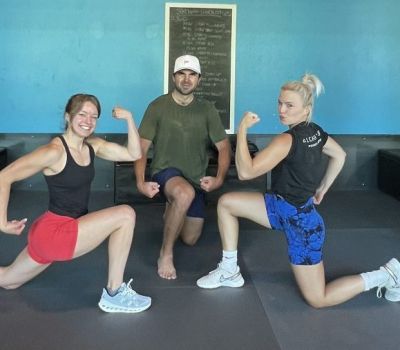 Three people flexing biceps. One woman in red shorts, one in blue, and a man kneeling in front.