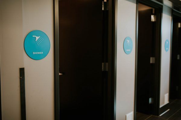 Row of shower room doors, each with a turquoise sign and white graphic on a neutral wall.