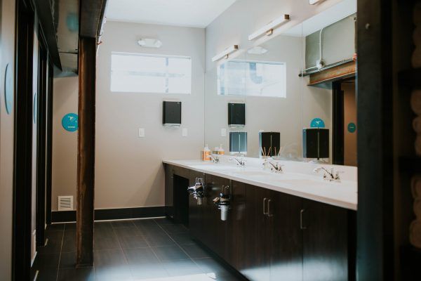 A public restroom with a long counter, sinks, and mirrors. Dark cabinets and gray walls.