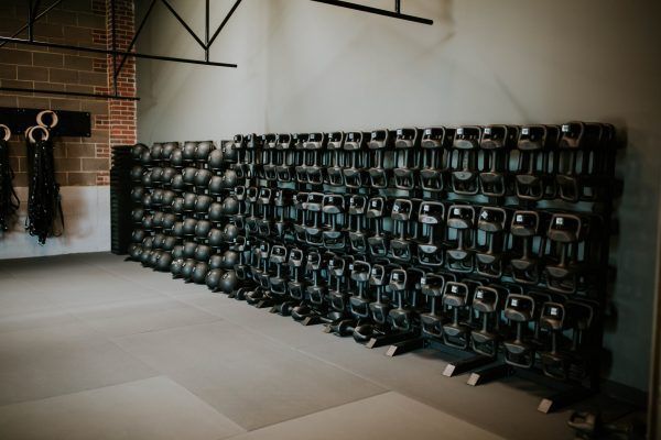 Rows of black kettlebells neatly arranged on racks in a gym.