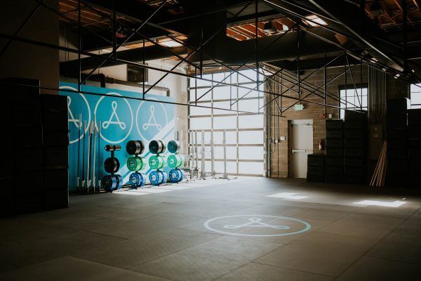 An empty gym with weights and equipment. Open door and a logo on the floor.