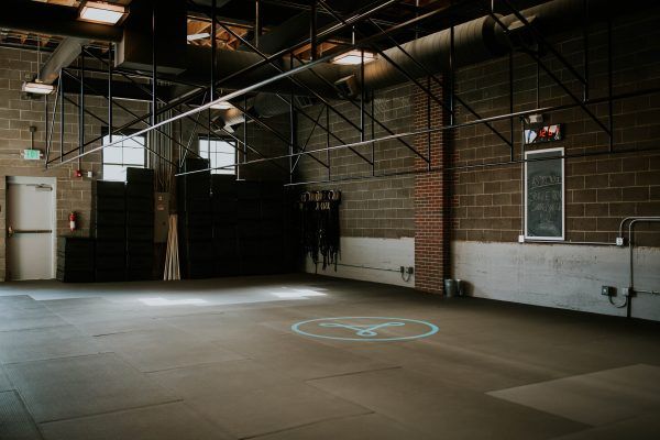 Empty warehouse space with exposed brick walls, fluorescent lights, and a projected symbol on the floor.