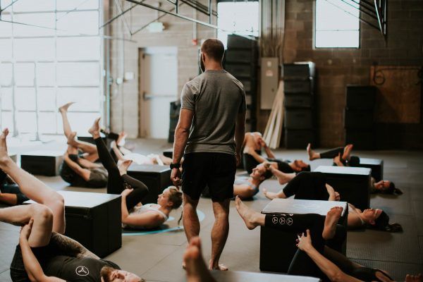 Instructor watches as people do floor exercises in a large gym.