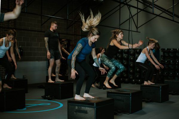 People jumping on boxes in a gym; dark gray walls, light blue floor detail.