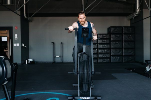 Man, Conor McGregor, exercising on a Rogue Echo bike in a gym setting.