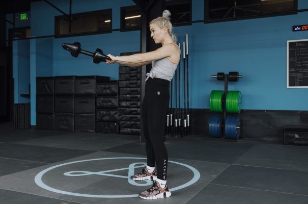 Woman in gym performs dumbbell exercise, extending arms forward.