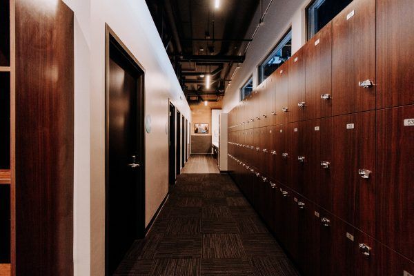 Hallway with wooden lockers on the right, dark doors on the left, and carpeted floor.