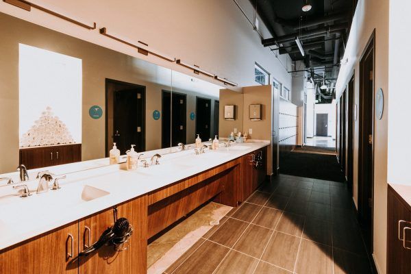 A modern, well-lit public restroom with a long counter of sinks, large mirror, and individual stalls.