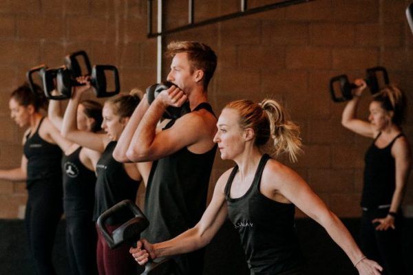 People exercising with weights in a gym, performing overhead presses.