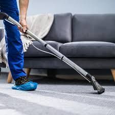 Person vacuuming a rug with an industrial cleaner near a gray couch.