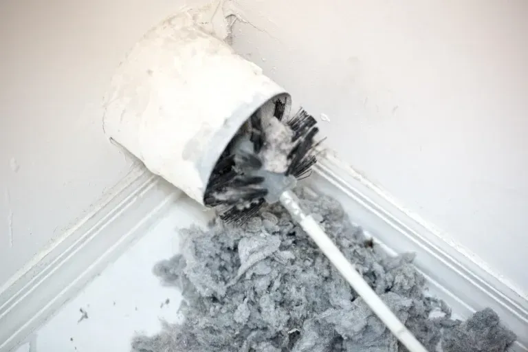 Cleaning dryer vent with brush, grey lint pile in front.