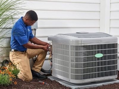 HVAC technician kneeling by an air conditioning unit, working on wires outdoors.