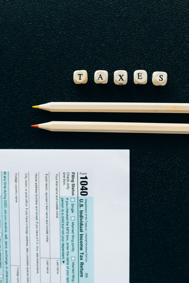 Tax form 1040, pencils, and letter blocks spelling "TAXES" on a dark surface.