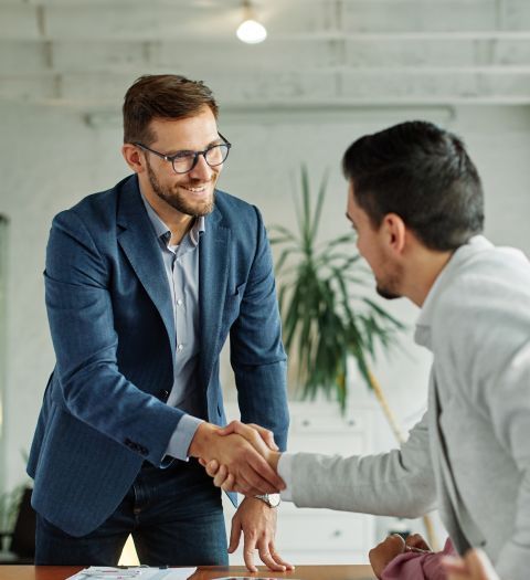 Two men shaking hands, one smiling, in an office.