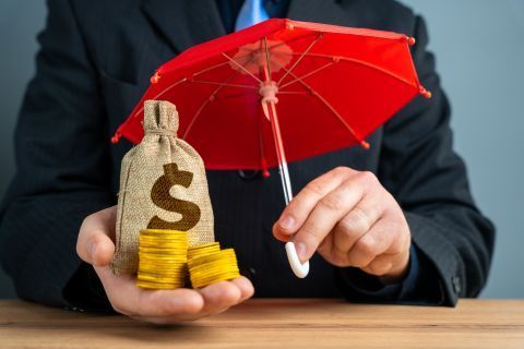 Person holding money bag and coins under a red umbrella, symbolizing financial protection.