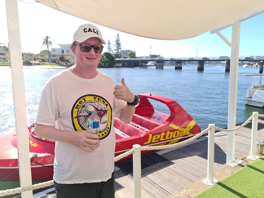 Man Standing in Front of Water Jet Boat, Smiling and Giving Thumbs Up - Comfort N Care Support QLD PTY LTD