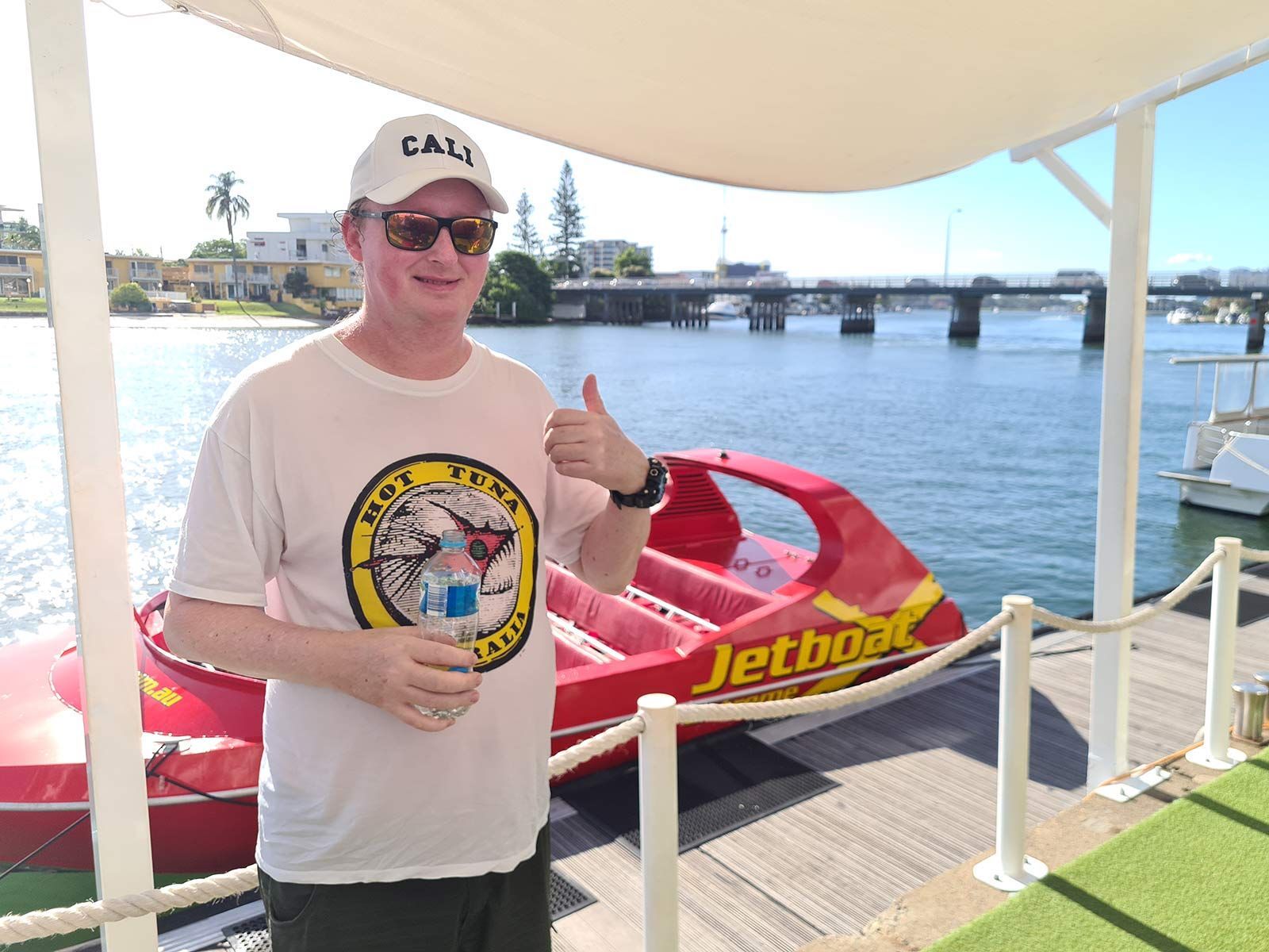Man Standing Front of a Water Jet Boat, Smiling and Giving a Thumbs up - Comfort N Care Support QLD PTY LTD