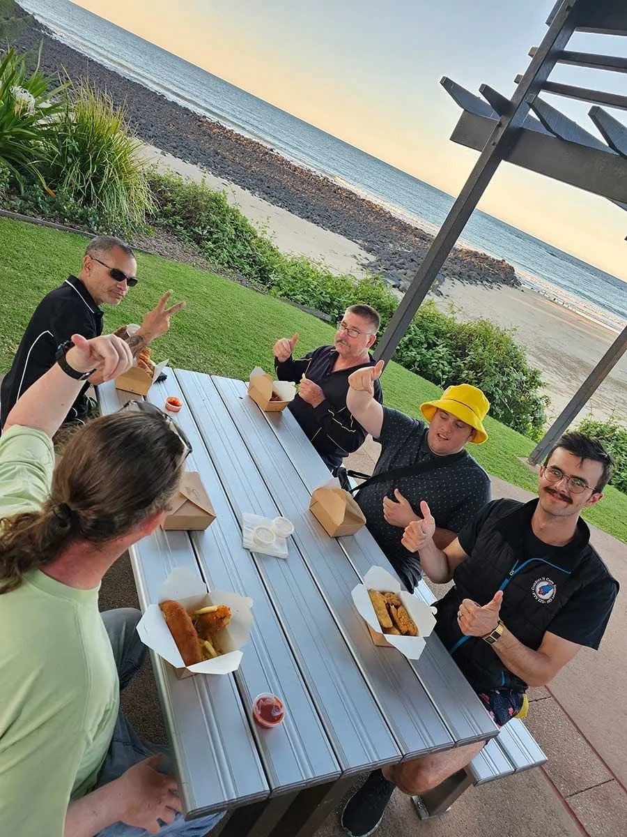 A Group of People Are Sitting at A Picnic Table Eating Food — Comfort N Care Support QLD Pty Ltd In Toowoomba City, QLD
