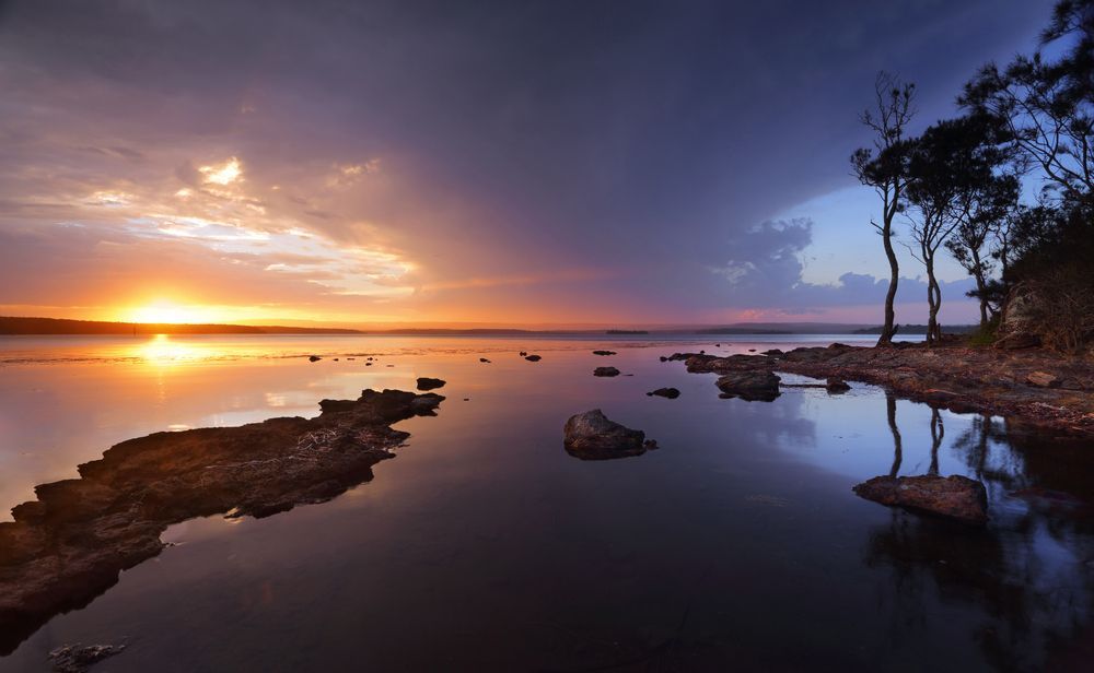 Sunset Over A Body Of Water With Rocks And Trees In The Background — Comfort N Care Support QLD Pty Ltd In St George, QLD