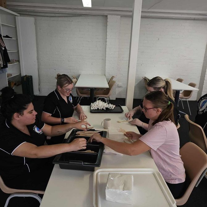 A Group of People Are Sitting Around a Table Eating Food — Comfort N Care Support QLD Pty Ltd In Toowoomba City, QLD