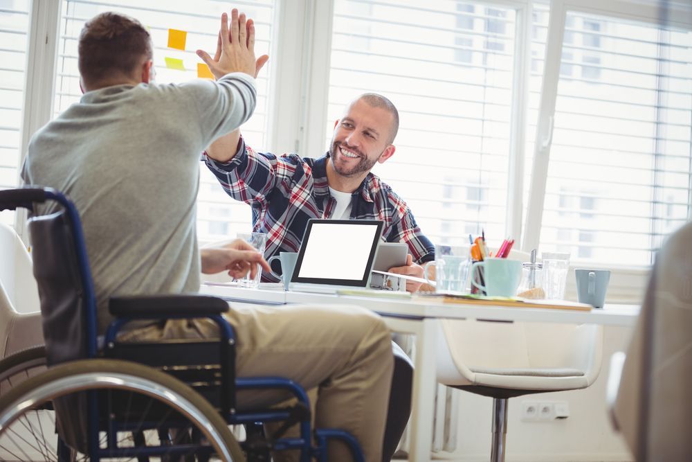 A Man In A Wheelchair Is Giving A High Five To Another Man — Comfort N Care Support QLD Pty Ltd In Highfields, QLD