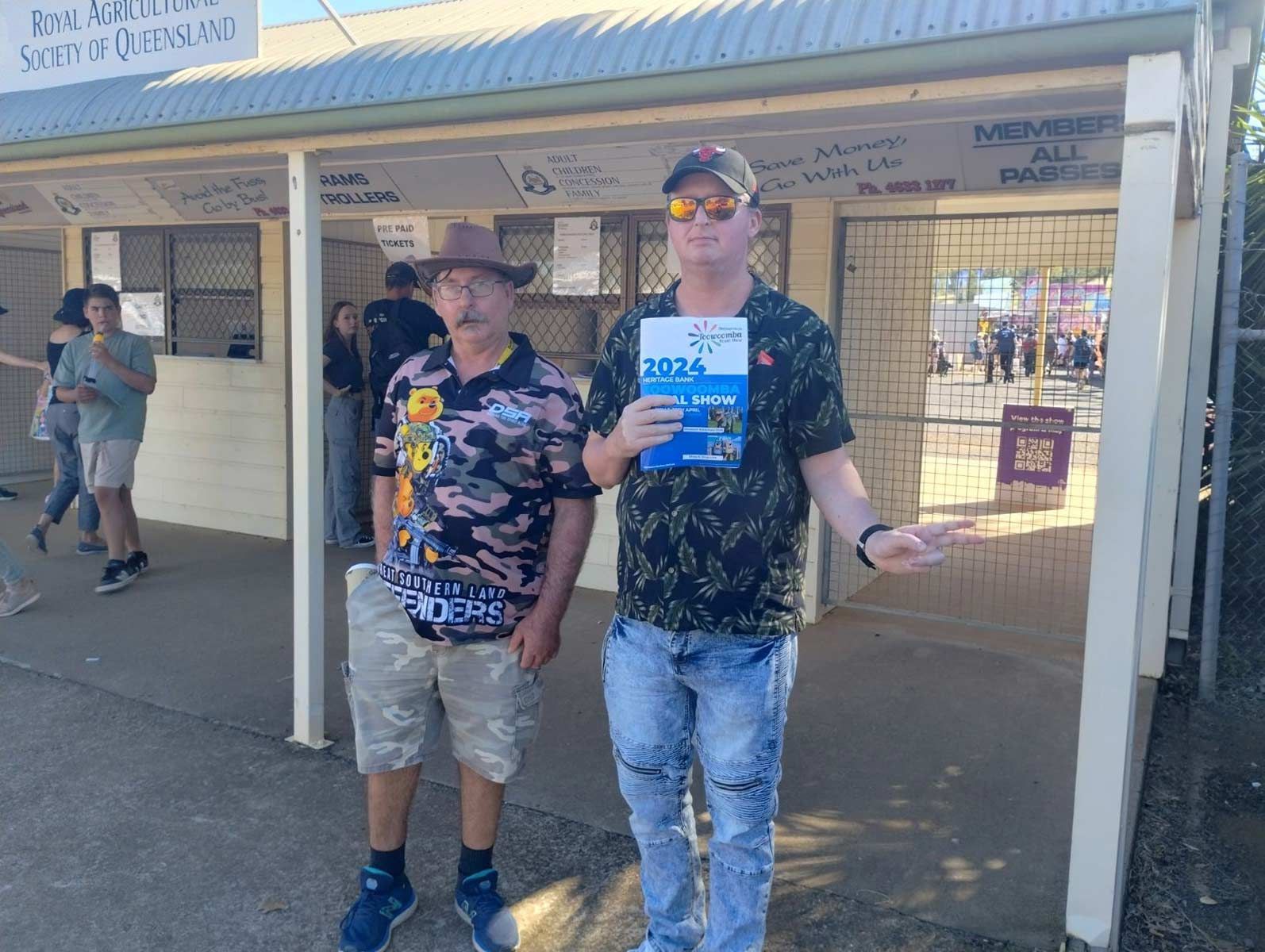 Two Men Are Standing Next to Each Other in Front Of a Building Holding a Book — Comfort N Care Support QLD Pty Ltd In Highfields, QLD