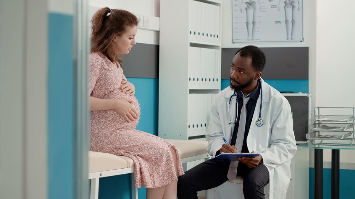 Uma mulher grávida está sentada em uma mesa conversando com um médico.