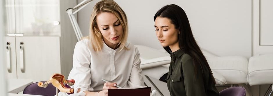 Duas mulheres estão sentadas à mesa olhando para um tablet.