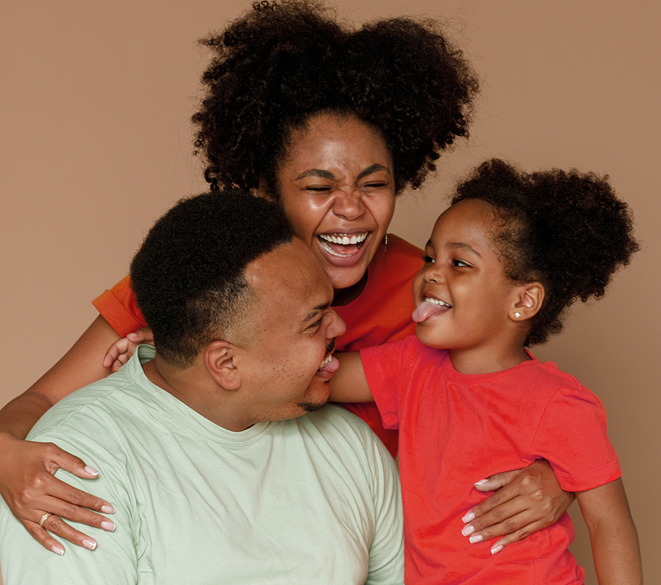 Um homem, uma mulher e uma criança riem juntos e a menina mostra a língua.