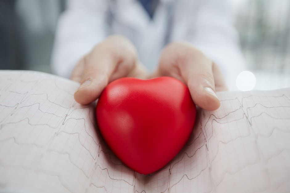 Um médico está segurando um coração vermelho nas mãos sobre um gráfico de ecg.