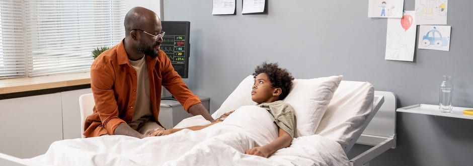 Um homem está sentado ao lado de uma criança em uma cama de hospital.