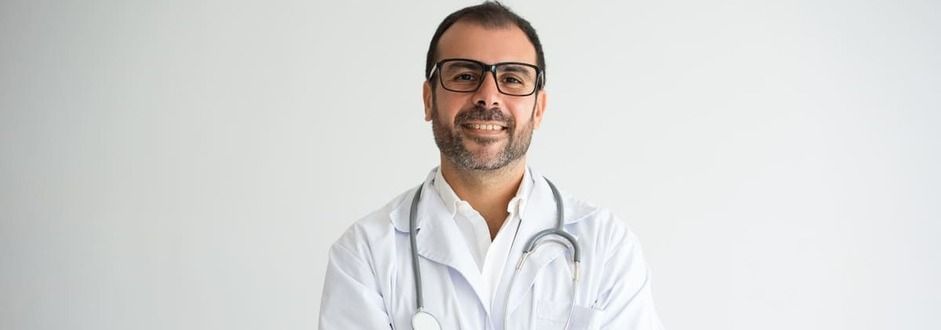 Um médico com um estetoscópio no pescoço está sorrindo com os braços cruzados.