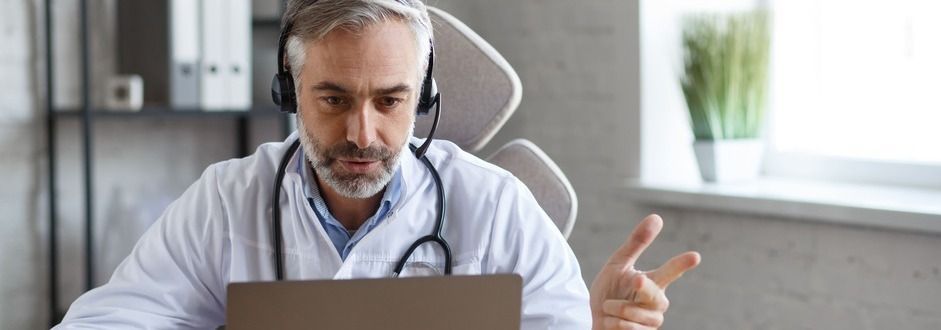 Um médico usando fones de ouvido está sentado em frente a um laptop.